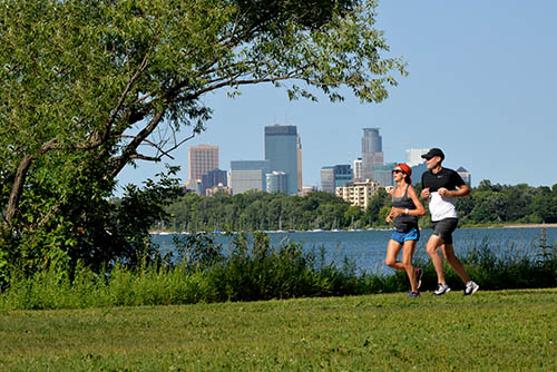 People jogging next to a lake, with the Minneapolis skyline in the background.