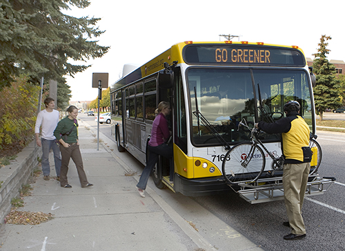 People boarding a bus while another rider removes their bike from the bike rack.