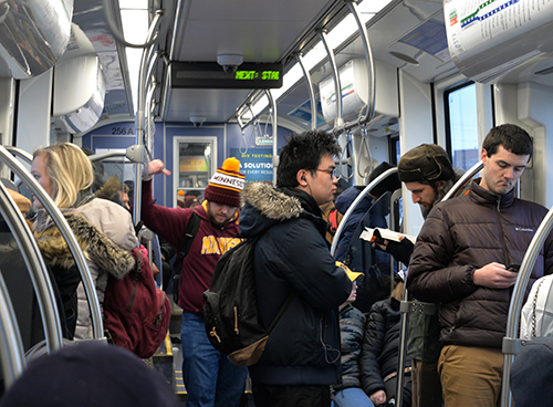 Several people standing inside a crowded light rail train.