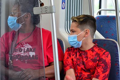 Two people wearing masks on the light rail.