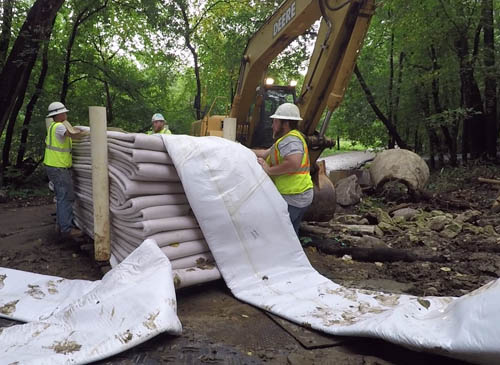 Three workers unfold the liner material for rehabilitating a large sewer pipe.