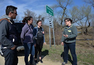 4 people talking at the edge of a road, next to a Vermillion River sign.