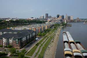 Housing development next to the river with barges, with downtown Saint Paul in the background.
