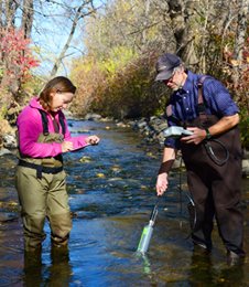 Two people testing stream water quality.