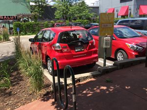 This car sharing vehicle is located in a commercial parking lot, along a transit route, and next to a bicycle rack.