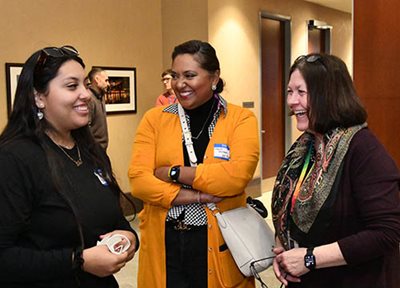 One Met Council member and two representatives from Mi C.A.S.A are having a conversation in the lobby, facing the Met Council chambers.