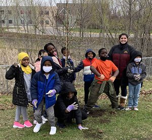 8 students and a teacher smiling with a small tree.