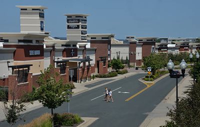 People crossing a street toward an outlet mall.
