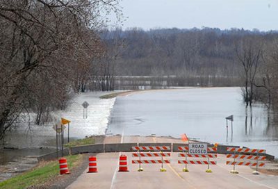 Road closed signs blocking a road, with water almost entirely covering the background.