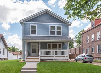 A light blue, 2-story, single-family home with a front porch.