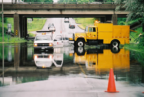 Two trucks in standing water on a paved road.