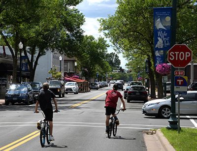 Two children biking on a tree-lined downtown street.