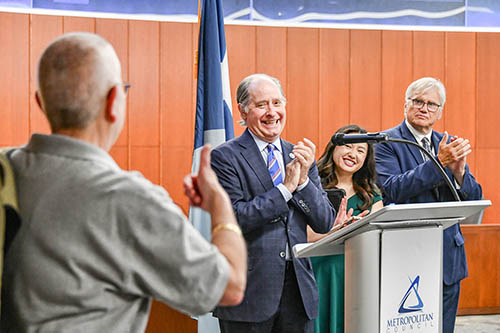 One person giving a thumbs up to three people standing behind a podium.