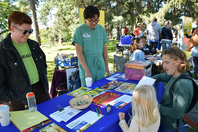 Woman and child at table staffed by two Met Council employees fill out a postcard.