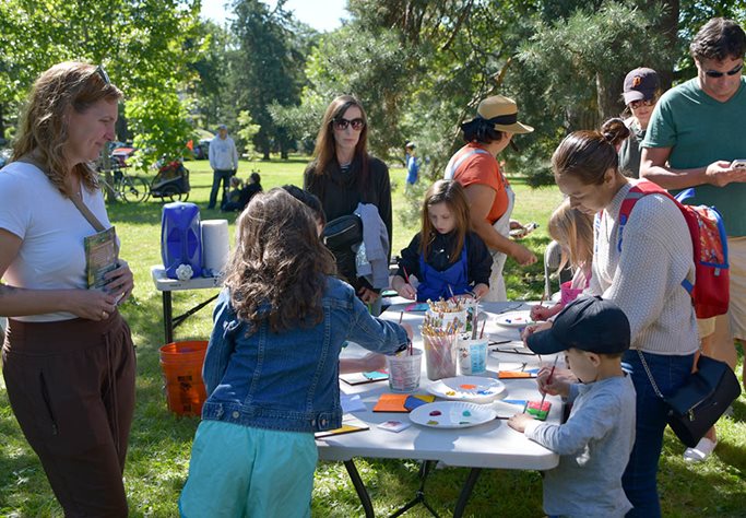 People stand around a table with paints and paintbrushes, painting tiles in bright colors.