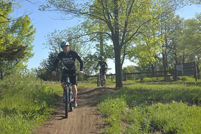 Man on off-road dirt bike trail followed by another cyclist.