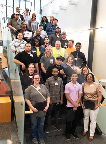 More than two dozen people posing on a staircase with cerificates.