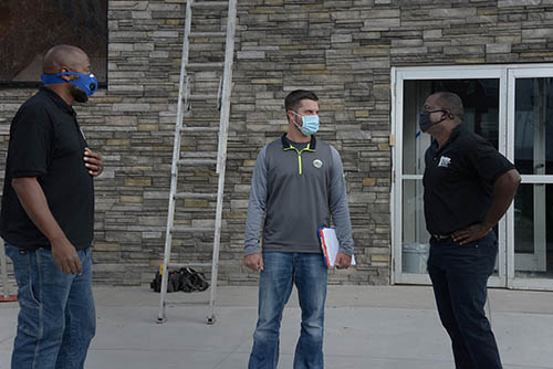 Three people in masks talking outside a brick building.