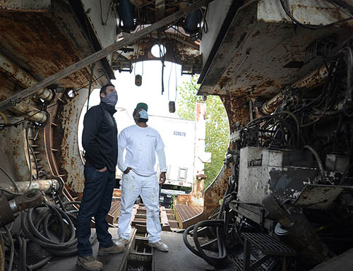 Two people with masks inside a giant tunnel boring machine.
