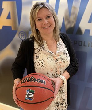 Elaine Ogilvie at Final Four headquarters. A woman posing with a basketball in front of a Final Four banner.