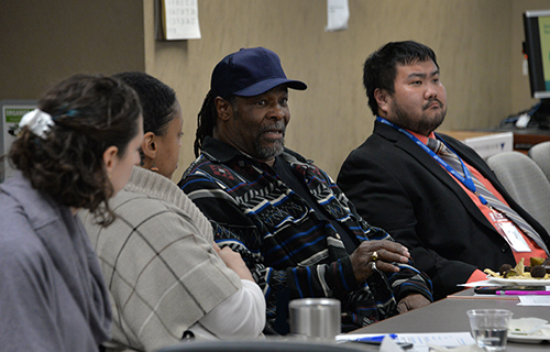 Three people listening to a person speaking at a table.