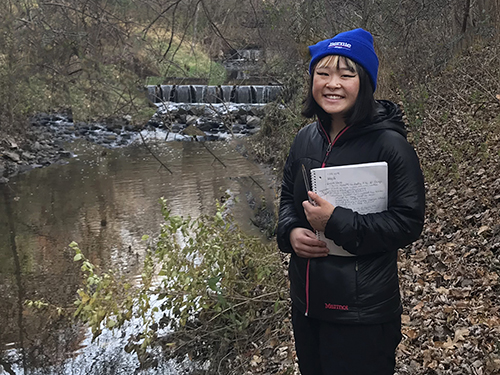 An intern with a notepad next to a creek.