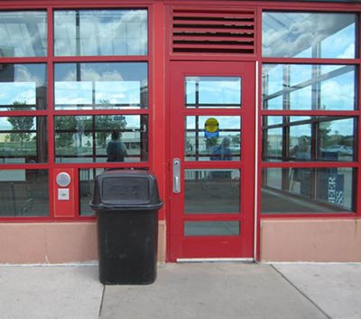 A trash can between a door and the button to open the door.