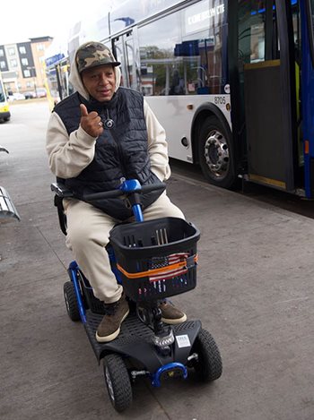 Someone giving a thumbs up next to a bus. They are on a motorized scooter.