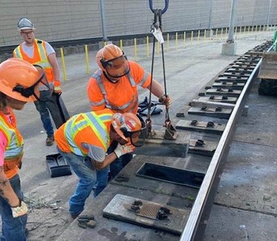 Four employees with tools work to repair light rail tracks.
