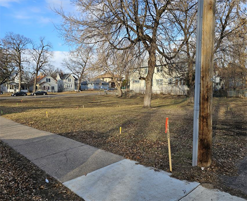 Vacant land at 1036 Marshall Avenue in Saint Paul, with houses on an adjacent street in the background.