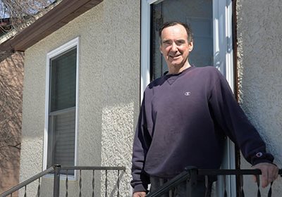 A man posing at the railing in front of a house.