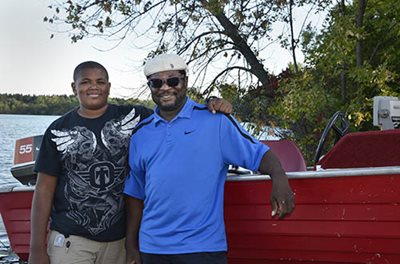 Two people posing in front of a boat by a lake.