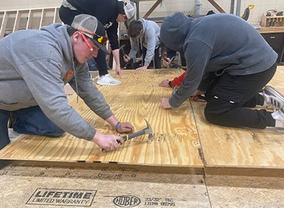 Students kneeling on boards hammering in nails.