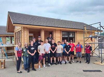 Group of students poses with adults in front of camper cabin with finished exterior.