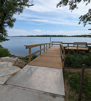 Steel ramp leads to wooden fishing pier on lake.