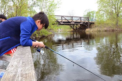 A child leaning on a concrete bridge with a fishing pole pointed toward the water.
