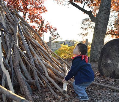 Small child positioning a log onto a large pile.
