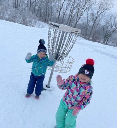 Two children cheering next to a disc golf target.