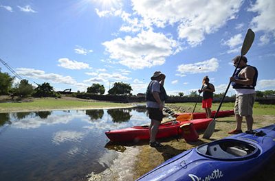 3 people preparing their kayaks next to the water.