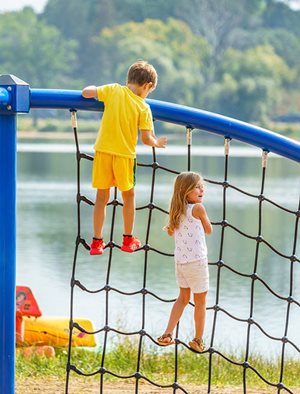 Two children climb at rope net with the lake in the background.