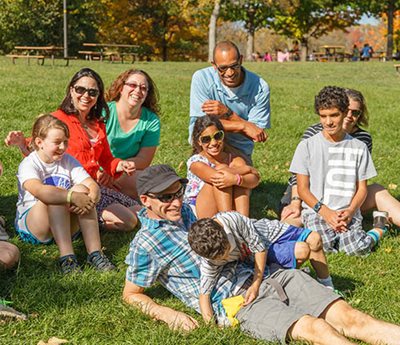 9 people laughing while sitting on the grass in a park.