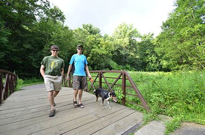 Two people and a dog walking across a bridge.