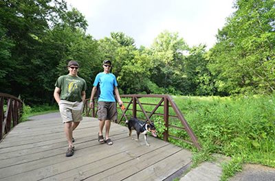 Two visitors walk their dog at Battle Creek Regional Park in Ramsey County. Battle Creek is one of several parks that will be expanded under the new parks plan. Two people and a dog walking across a bridge.