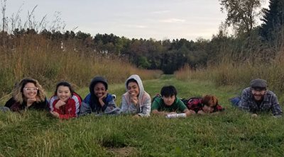 6 youth posing with an adult while lying on a grass path.