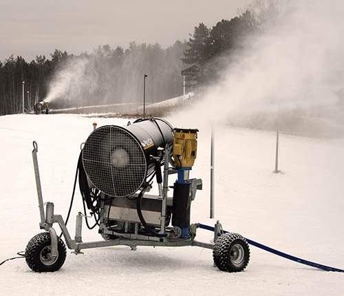 A snow-making machine sprays snow at a park.