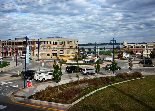 A traffic roundabout in Forest Lake, with businesses and the lake in the background.