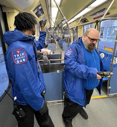 Two TRIP agents stand near door on light rail car.