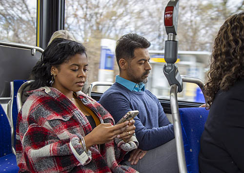 Two passengers seated on a Metro Transit bus look down at their cell phones.