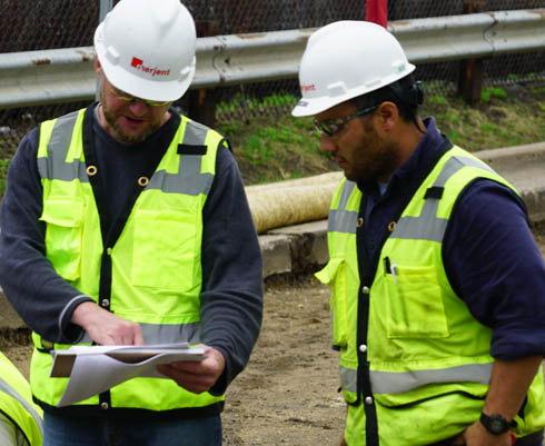 Two workers in green vests looking at papers.