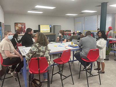 People sitting and standing in a room with several tables.